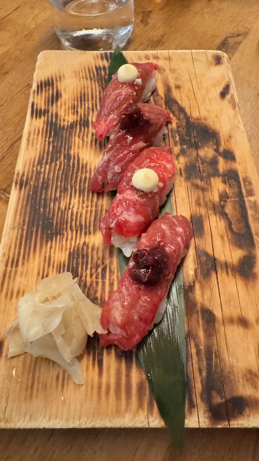 Τέσσερα κομμάτια nigiri με καμένο μοσχάρι σε καμένη ξύλινη σανίδα με πίκλα τζίντζερ, δύο με κρέμα από πάνω και δύο με σκούρο ρελίς