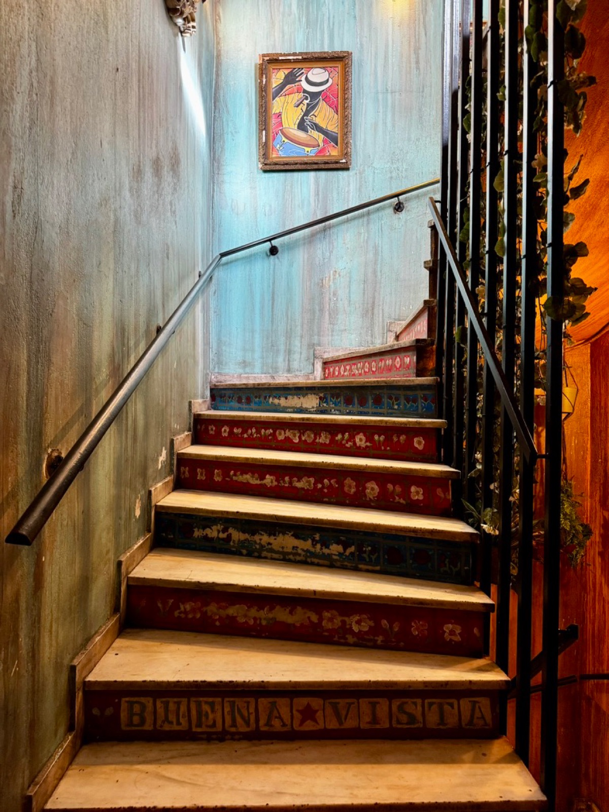 A tiled staircase with Buena Vista spelled on the risers and a painting of a drummer on the landing wall