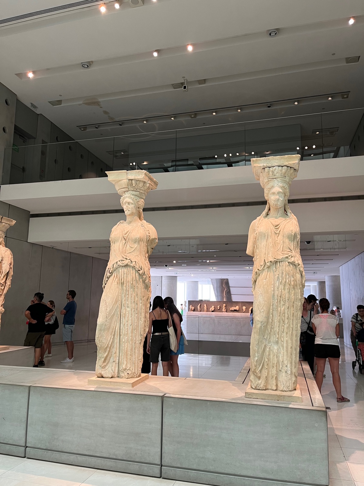 Οι αυθεντικές Καρυάτιδες εκτεθειμένες σε υπερυψωμένο βάθρο μέσα στο Μουσείο Ακρόπολης, επισκέπτες να τις κοιτάζουν από κάτω
