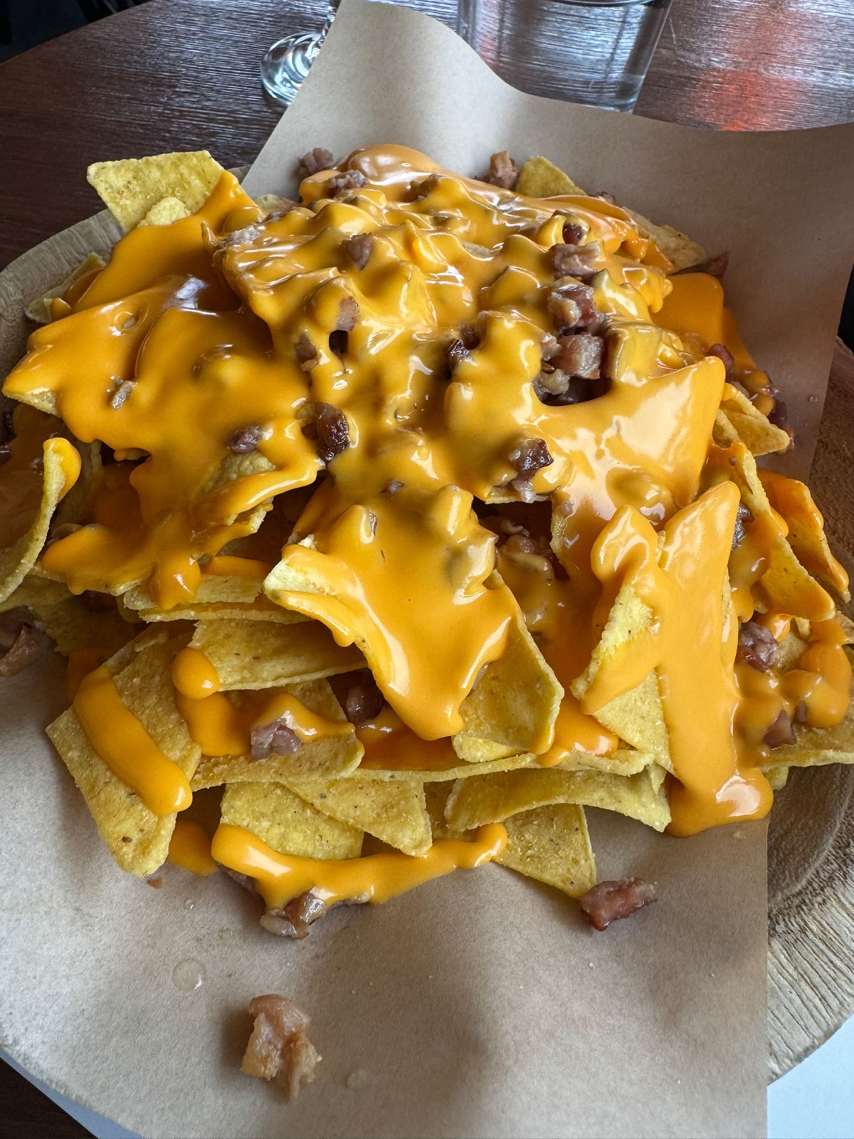 A plate of nachos covered in melted cheese sauce with bacon pieces and herbs