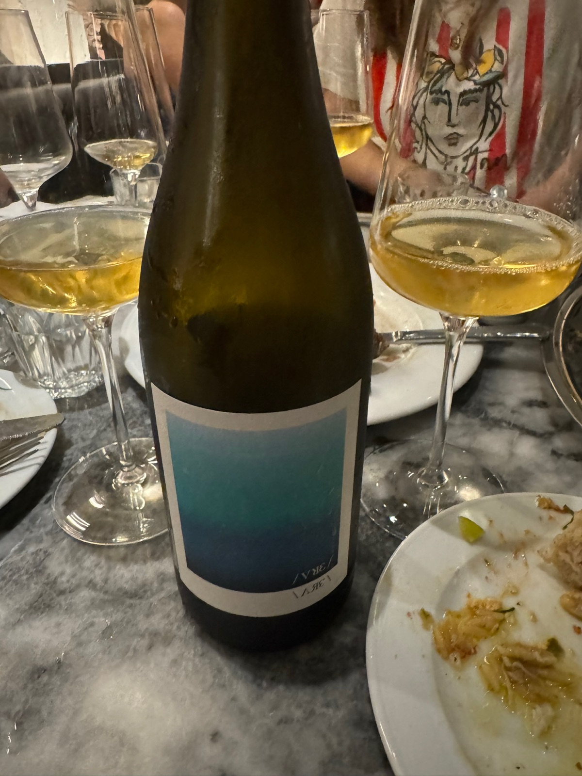 A wine bottle with a blue gradient label next to two coupe glasses on a wooden bar counter