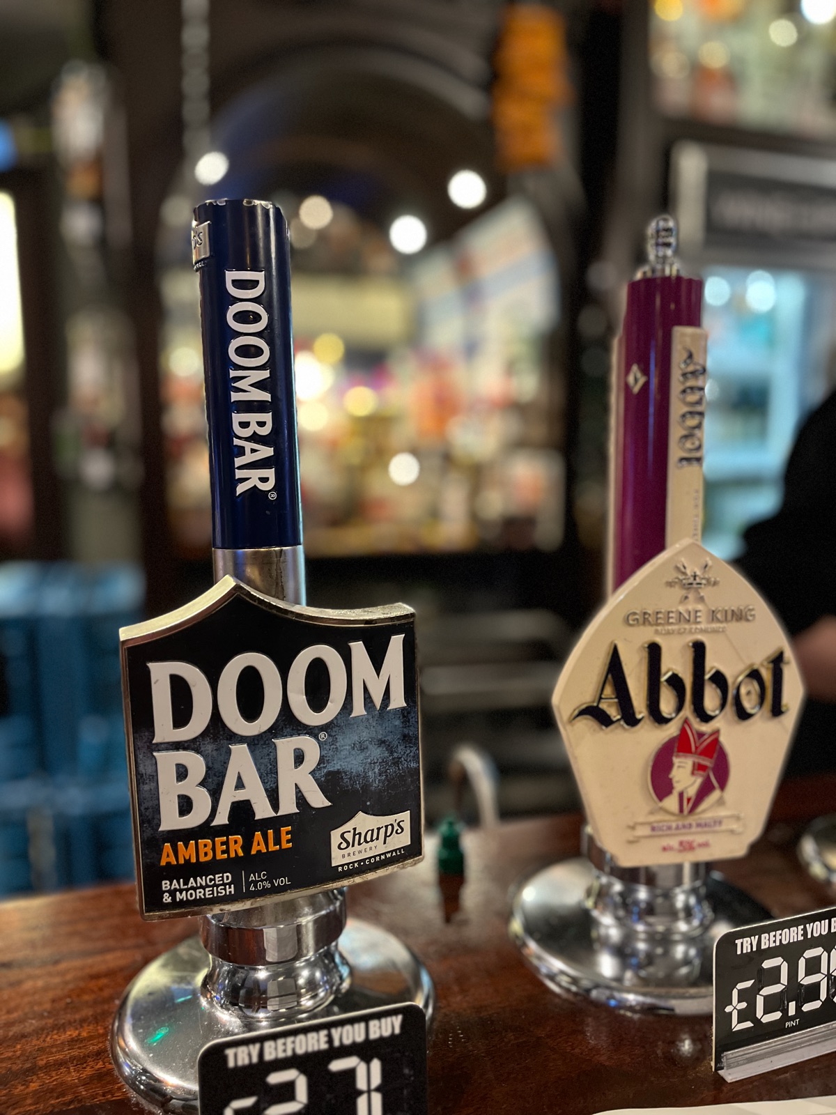 Χειραντλίες Doom Bar και Greene King Abbot σε μπάρα παμπ, καθεμία με ένα μικρό ταμπελάκι try before you buy από κάτω