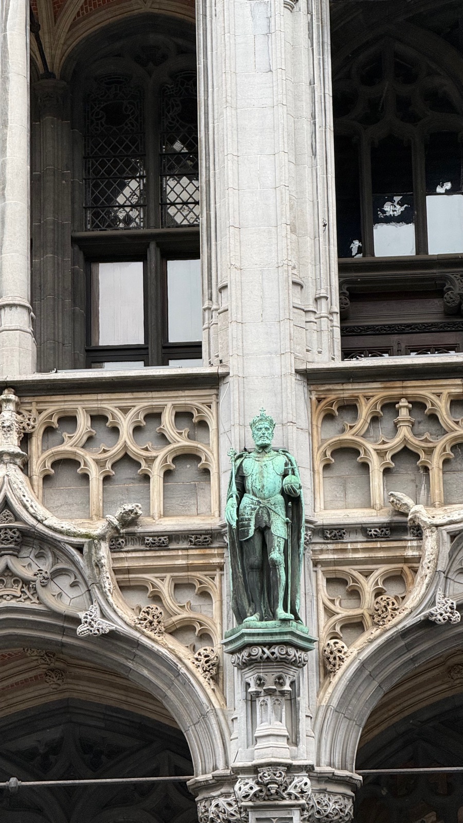 Λεπτομέρεια γοτθικής πρόσοψης στην Grand Place με ένα πράσινο χάλκινο άγαλμα στεμμένης μορφής με πανοπλία που κρατάει σφαίρα και σκήπτρο ανάμεσα σε σκαλισμένες κορυφώσεις