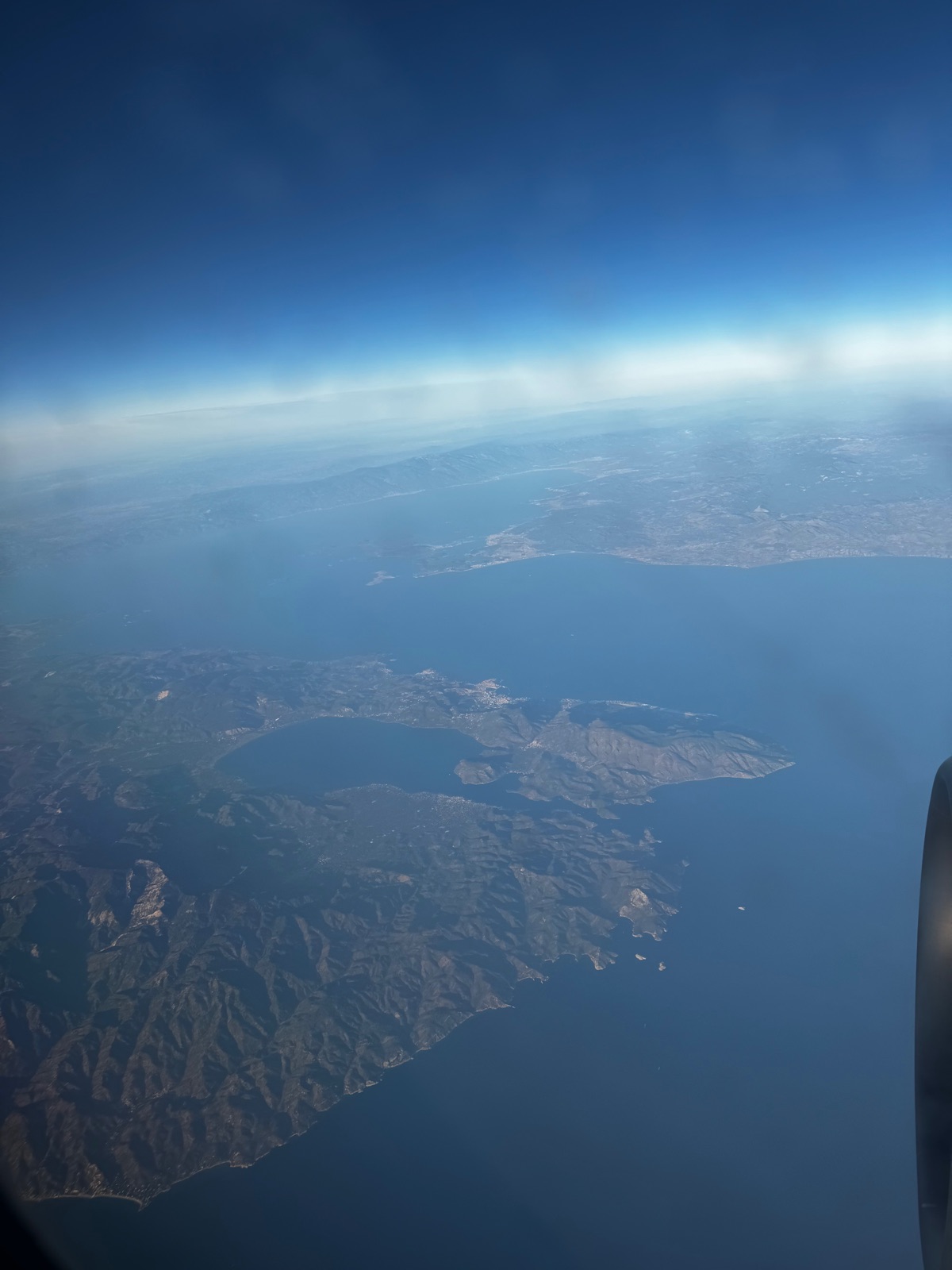 Η κυπριακή ακτή από παράθυρο αεροπλάνου, μια ορεινή ακτή με μια μεγάλη λίμνη κλεισμένη πίσω από στενή παράκτια λωρίδα, το κάλυμμα κινητήρα στην άκρη του κάδρου