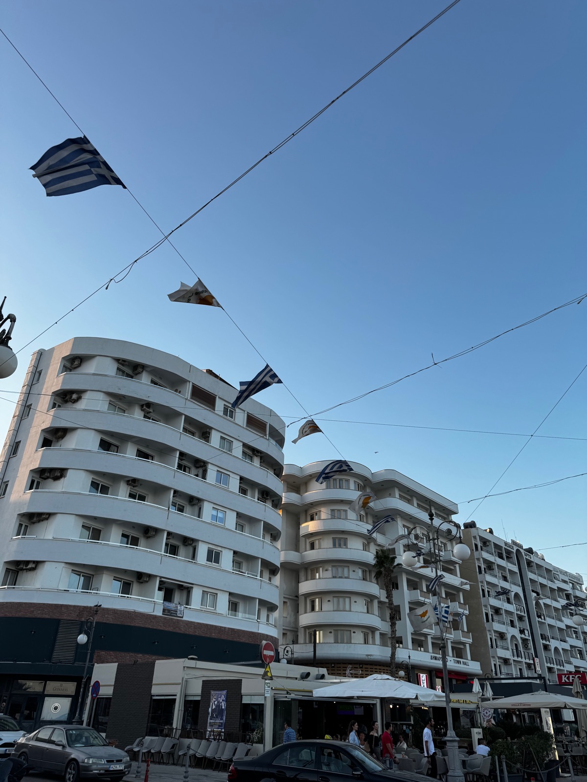 Το καμπύλο λευκό κτίριο του δημαρχείου στον περίπατο της Λάρνακας τη χρυσή ώρα, ελληνικές και κυπριακές σημαίες να κυματίζουν σε σύρματα και μπαλκόνια