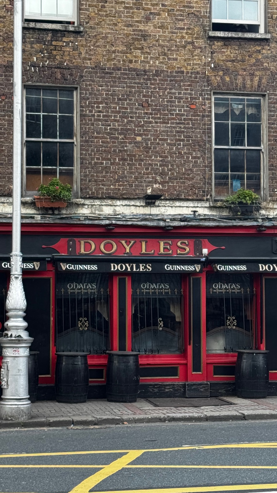 Η κόκκινη και χρυσή πρόσοψη της παμπ Doyle's σε δρόμο του Δουβλίνου, γράμματα Guinness σε όλο το μήκος, σκούρα παράθυρα κάτω από τούβλα