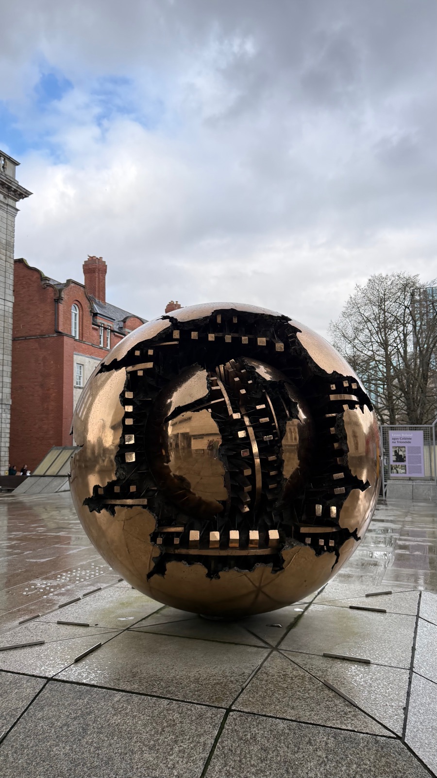 Κοντινή λήψη του χάλκινου γλυπτού στο Trinity College, το ραγισμένο εξωτερικό του κέλυφος να καθρεφτίζει τα γύρω κτίρια