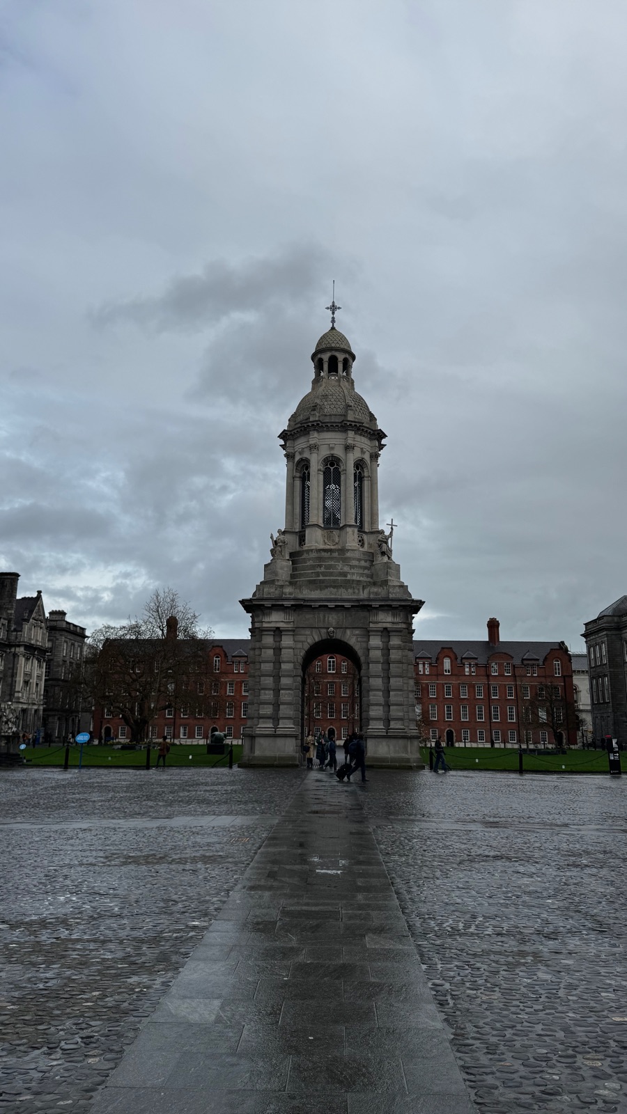 Το πέτρινο Campanile στο Trinity College να στέκεται μόνο του στην Parliament Square, βρεγμένα βότσαλα να καθρεφτίζουν τον γκρίζο ουρανό, κόκκινα τούβλινα κτίρια πίσω