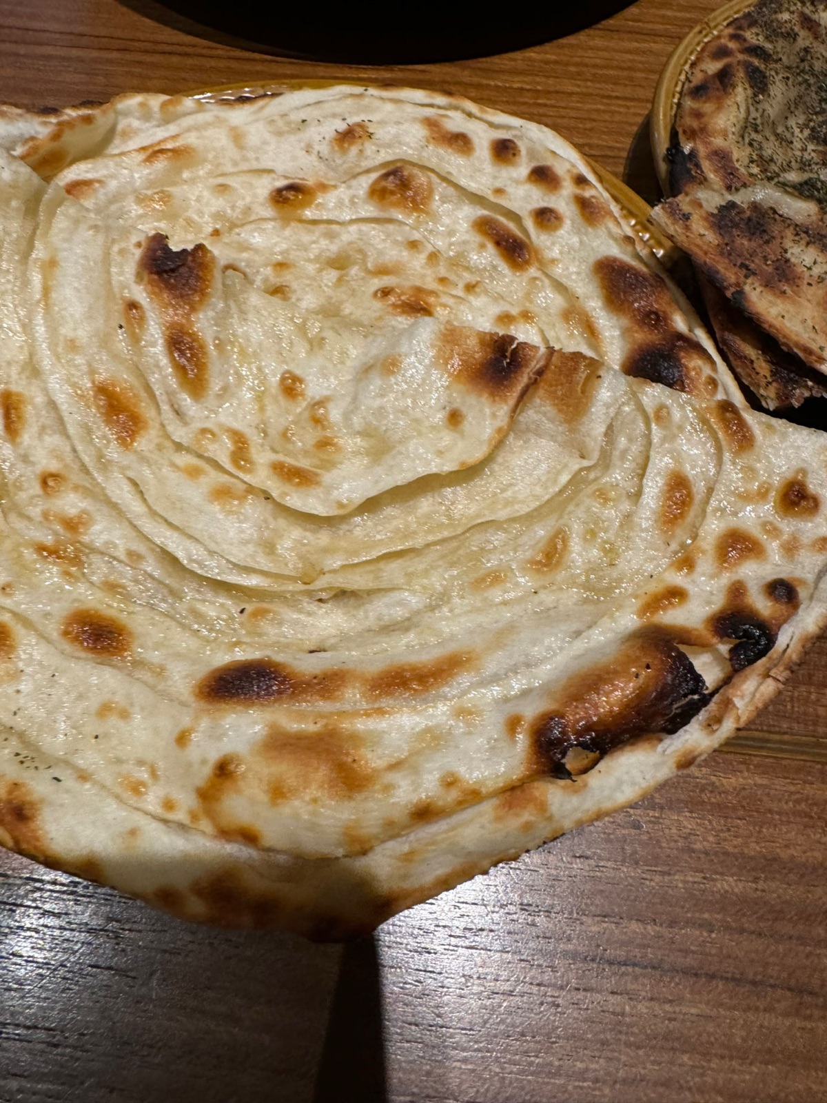 Κοντινό μιας φυλλωτής σπιράλ laccha paratha με καψαλισμένα σημεία και ένα ρότι tandoori πασπαλισμένο με δυόσμο δίπλα της