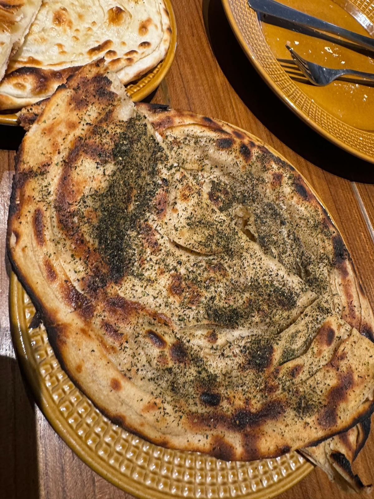 Στρωματωμένη paratha πασπαλισμένη με δυόσμο και μυρωδικά σε ένα ώχρα πιάτο με ναν πίσω