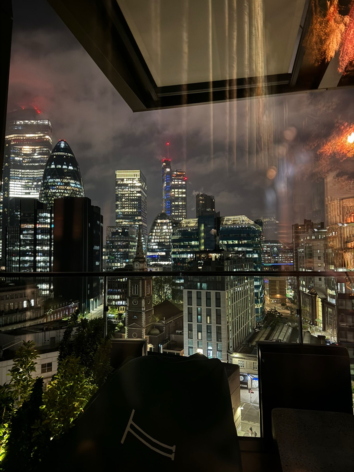 Νυχτερινή θέα από ένα roof bar πάνω από το City of London, το Gherkin και οι γύρω πύργοι φωτισμένοι, ένας πύργος εκκλησίας σκοτεινός στο πρώτο πλάνο