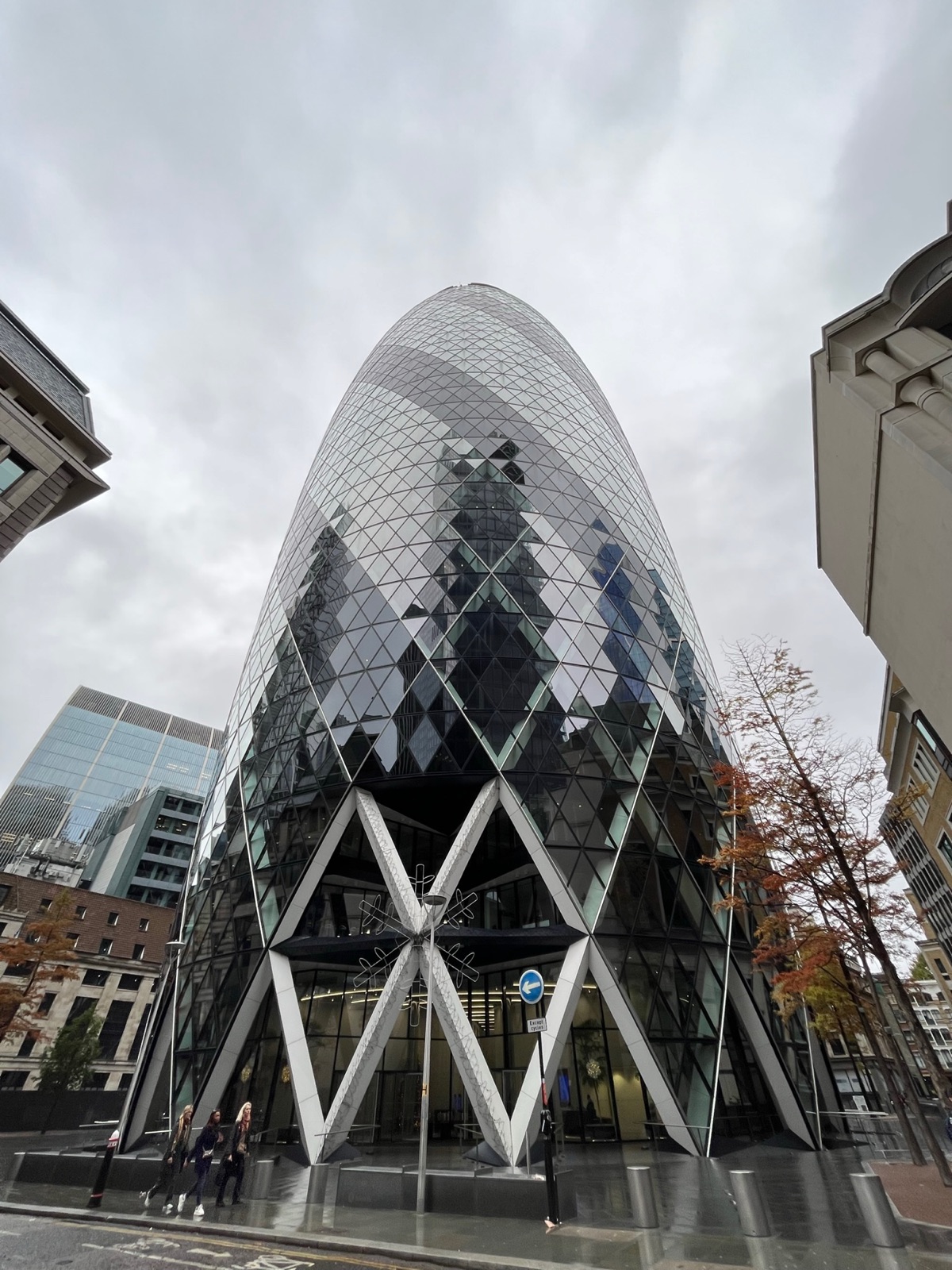Το Gherkin σε επίπεδο δρόμου με μια μεγάλη διακοσμητική νιφάδα κρεμασμένη στις καμάρες της εισόδου του, κόσμος να διασχίζει τον βρεγμένο δρόμο