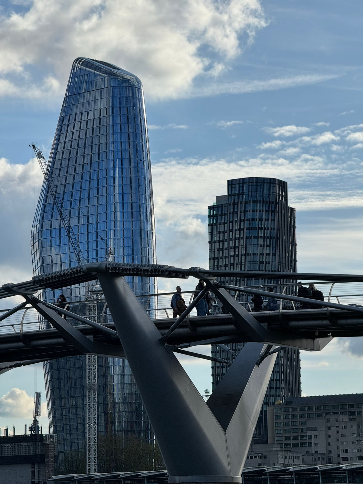Η Millennium Bridge με πεζούς να τη διασχίζουν, ο καμπύλος γυάλινος πύργος One Blackfriars και ο South Bank Tower πίσω κόντρα σε γαλάζιο ουρανό