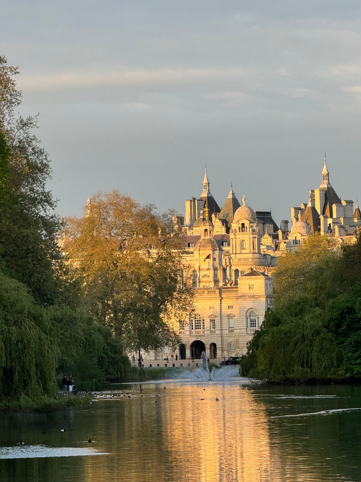 Η λίμνη στο St James's Park την ώρα του χρυσού φωτός, ένα σιντριβάνι στη μέση της λίμνης, οι τρούλοι και οι πυργίσκοι του Horse Guards να λάμπουν χρυσοί πέρα από τα δέντρα