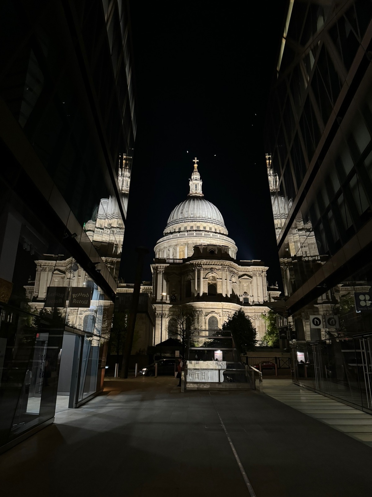 Ο τρούλος του καθεδρικού του St Paul's φωτισμένος τη νύχτα, πλαισιωμένος και αντανακλασμένος από τους σκούρους γυάλινους τοίχους του περάσματος One New Change