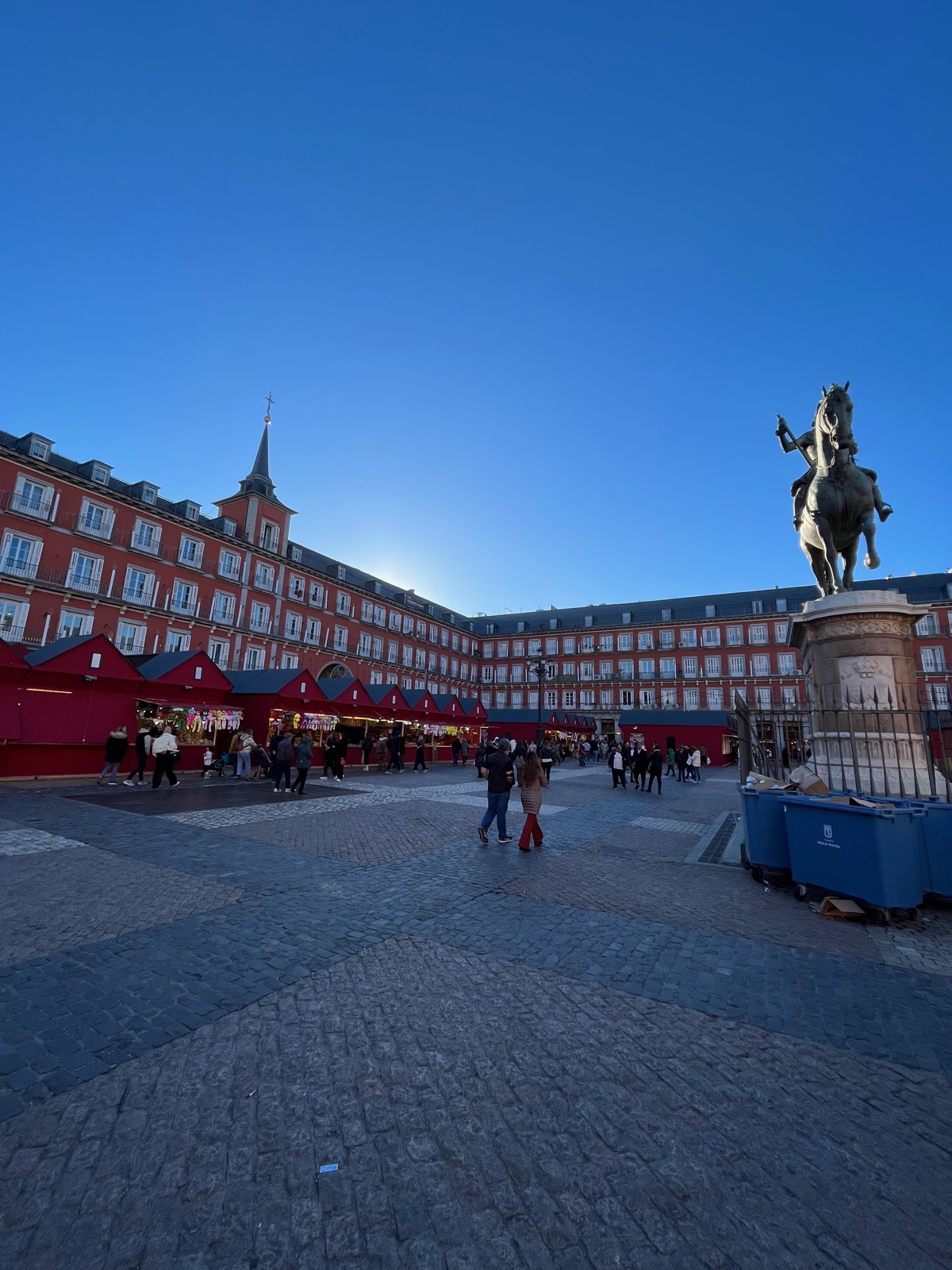 Η Plaza Mayor σε χαμηλό απογευματινό φως, πάγκοι χριστουγεννιάτικης αγοράς με κόκκινα καραβόπανα στα λιθόστρωτα και το έφιππο άγαλμα του Φιλίππου Γ' δεξιά