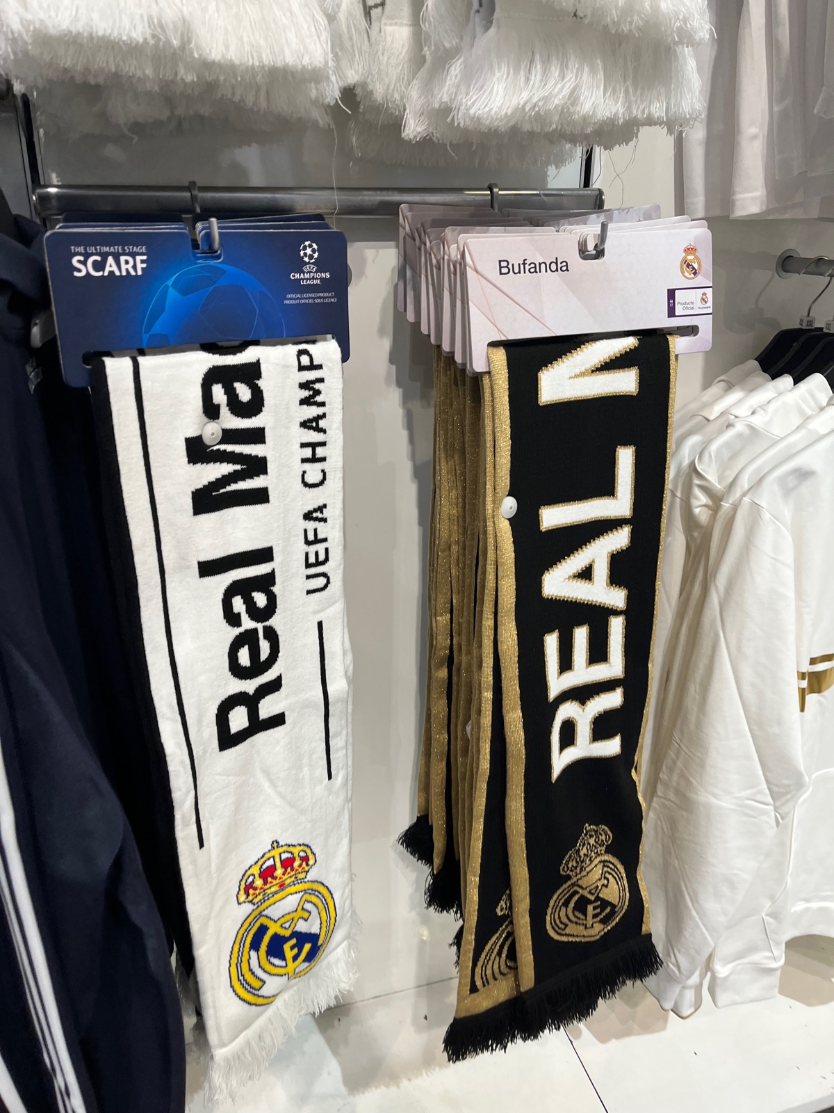 Κασκόλ UEFA Champions League της Ρεάλ Μαδρίτης κρεμασμένα σε κατάστημα του συλλόγου, ένα λευκό και ένα μαύρο με χρυσά γράμματα