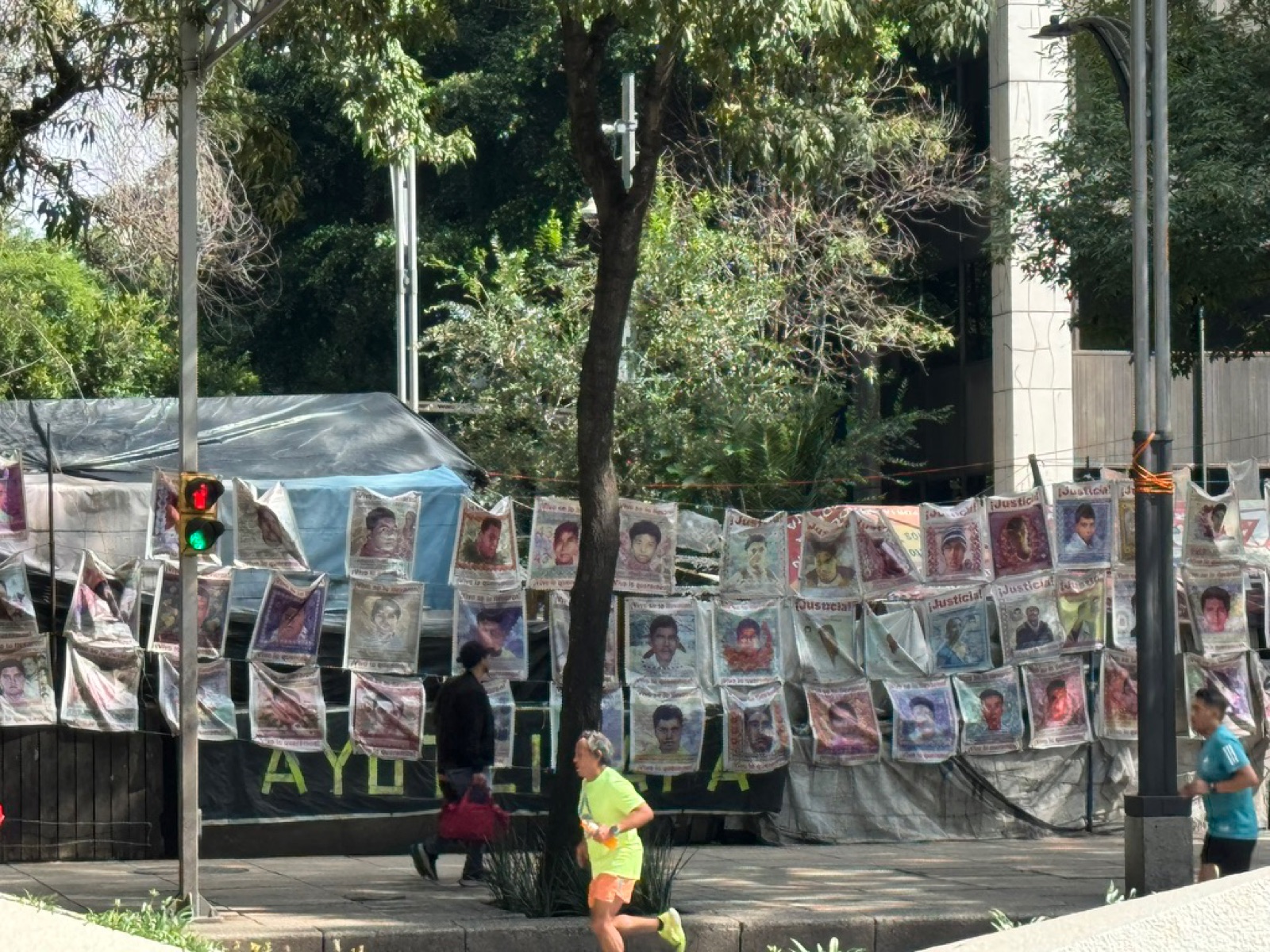 Ξεθωριασμένα πανό με πρόσωπα των φοιτητών της Αγιοτσινάπα σε έναν φράχτη καθώς δρομείς περνούν στην κυριακάτικη λεωφόρο χωρίς αυτοκίνητα