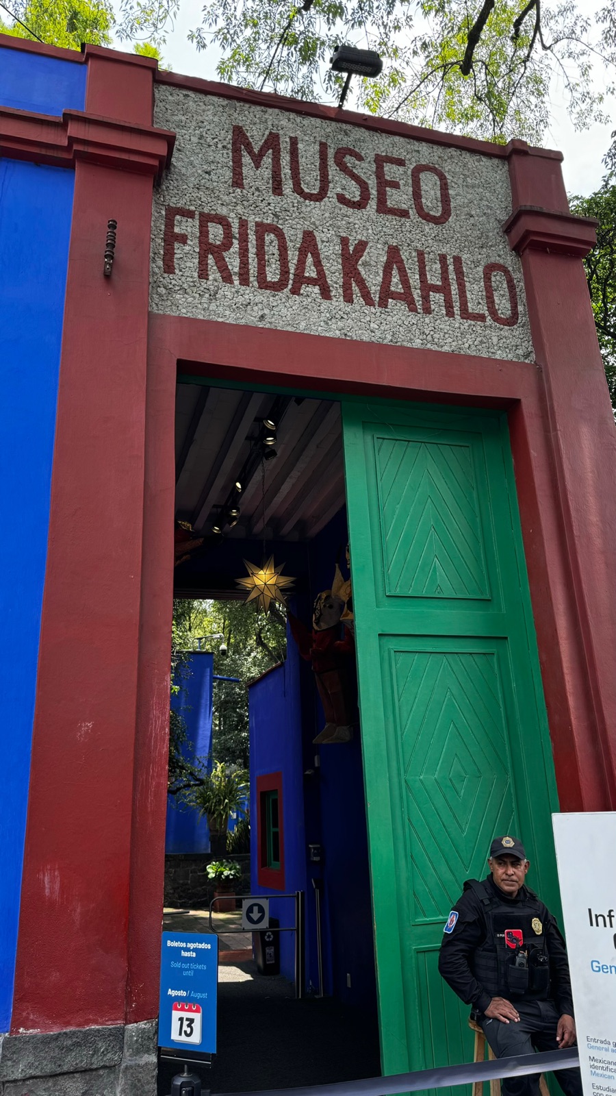 Η αψίδα εισόδου του Μουσείου Φρίντα Κάλο με την πέτρινη πινακίδα της, ανοιχτή πράσινη πόρτα και μια ανακοίνωση εξαντλημένων εισιτηρίων
