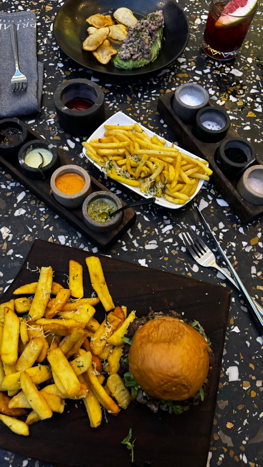 Ένα μπέργκερ steakhouse σε ένα ξύλινο ξύλο με τηγανητές πατάτες πασπαλισμένες με παρμεζάνα, σειρές σάλτσας και ταρτάρ αβοκάντο