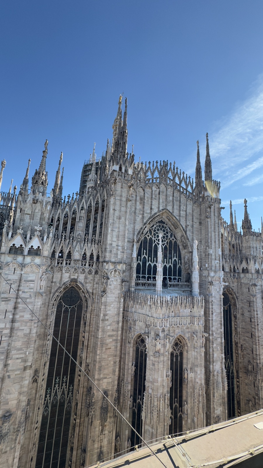 Κοντινή λήψη του μαρμάρινου πλαϊνού του Duomo πάνω σε βαθύ γαλάζιο ουρανό, σειρές από κορυφώσεις, αγάλματα και αντηρίδες σε ζεστό απογευματινό φως, σκαλωσιές γύρω από ένα καμπαναριό