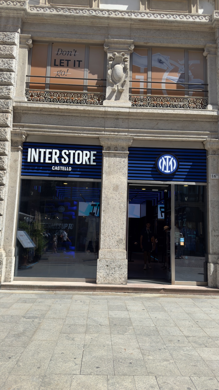Η πρόσοψη του Inter Store Castello στη Via Dante, μπλε και μαύρη ριγέ επιγραφή με το σήμα του συλλόγου ενταγμένο σε πέτρινο μέγαρο, το πεζοδρόμιο μπροστά σχεδόν άδειο