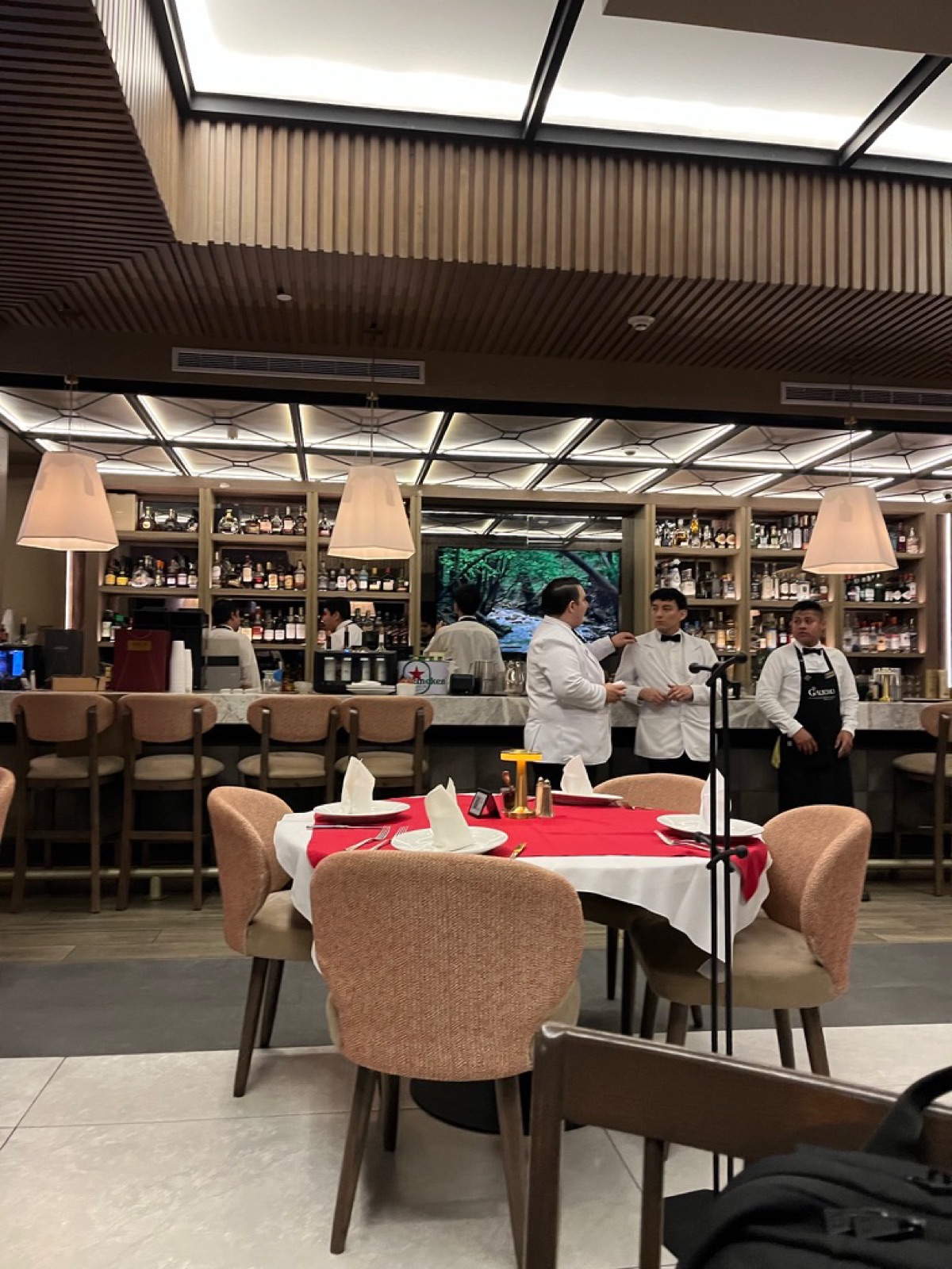 Σερβιτόροι με λευκά σακάκια όρθιοι στο φωτισμένο από πίσω μπαρ του steakhouse El Gaucho, ένα στρογγυλό τραπέζι με κόκκινο τραπεζομάντιλο στρωμένο μπροστά