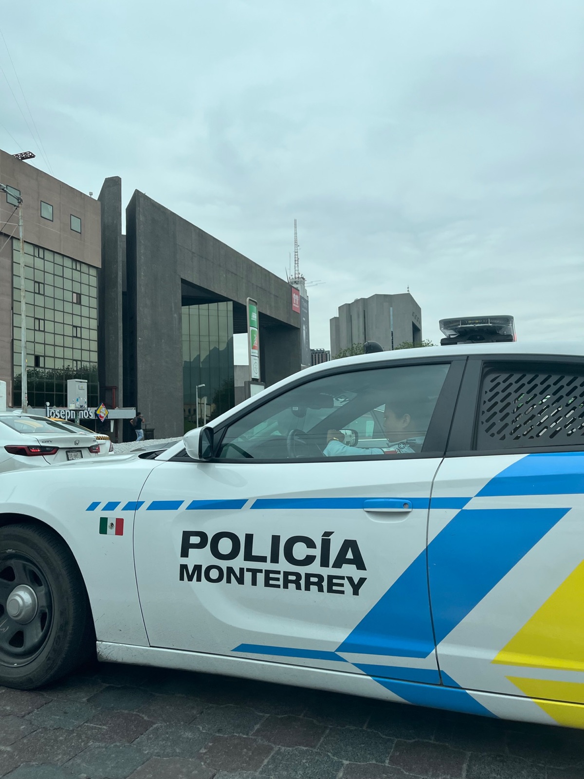 Ένα λευκό Dodge Charger της Policia Monterrey παρκαρισμένο μπροστά από ένα μπρουταλιστικό τσιμεντένιο κτίριο