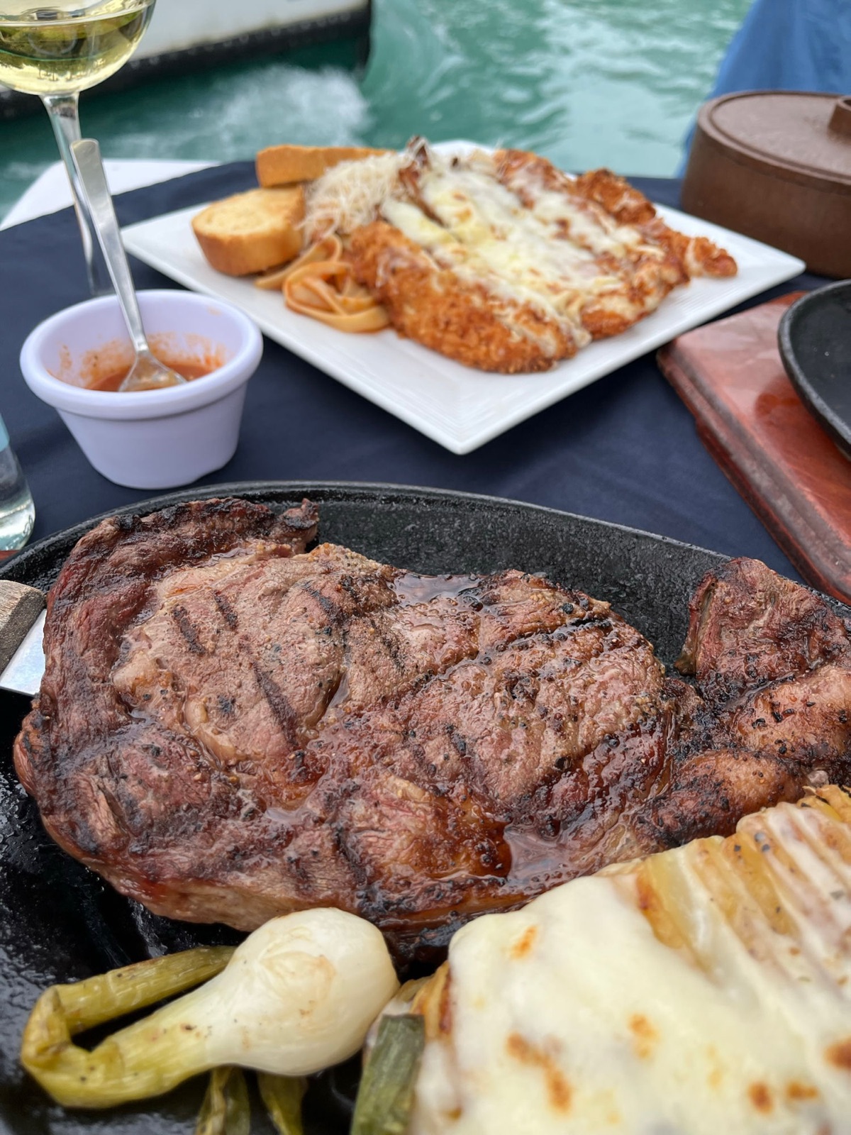 Ένα ψητό ribeye σε ένα τσιτσιριστό μαντεμένιο πιάτο με φρέσκα κρεμμυδάκια, το τιρκουάζ κανάλι πίσω