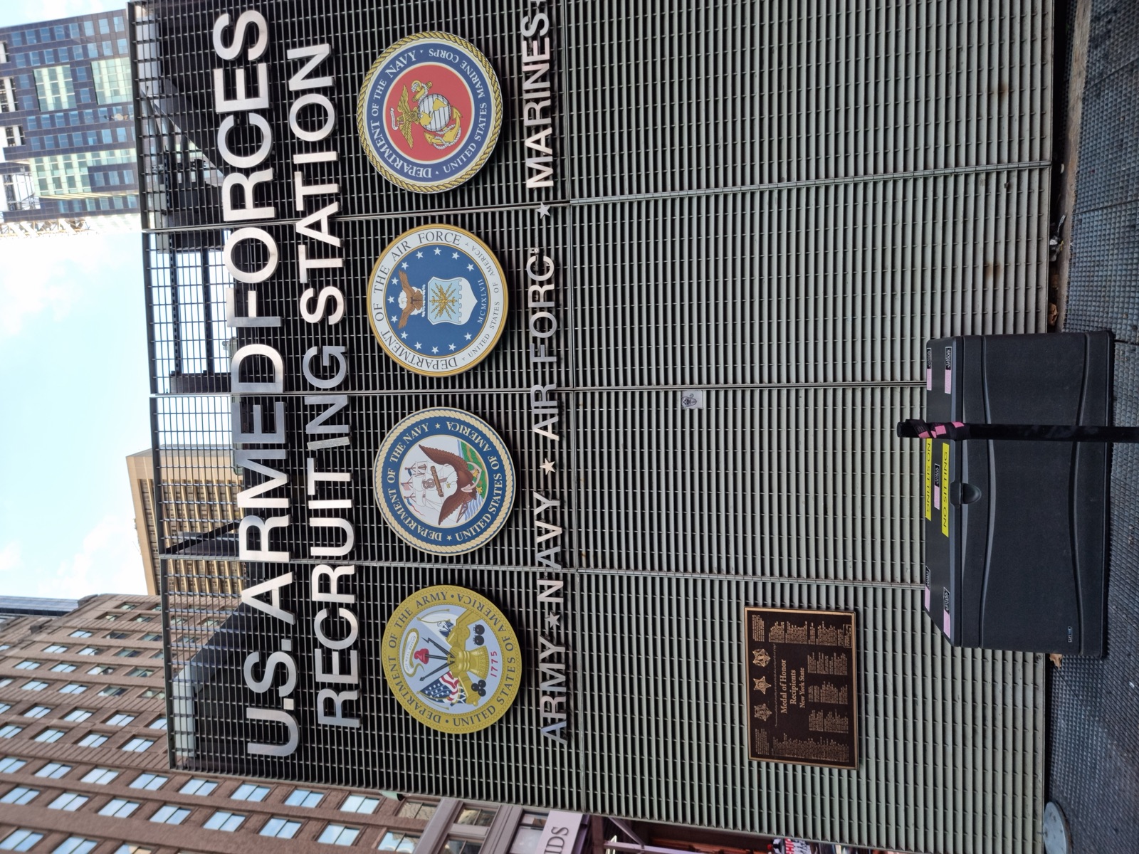 A metal-clad building front lettered U.S. ARMED FORCES RECRUITING STATION with the seals of the Army, Navy, Air Force and Marines beneath it