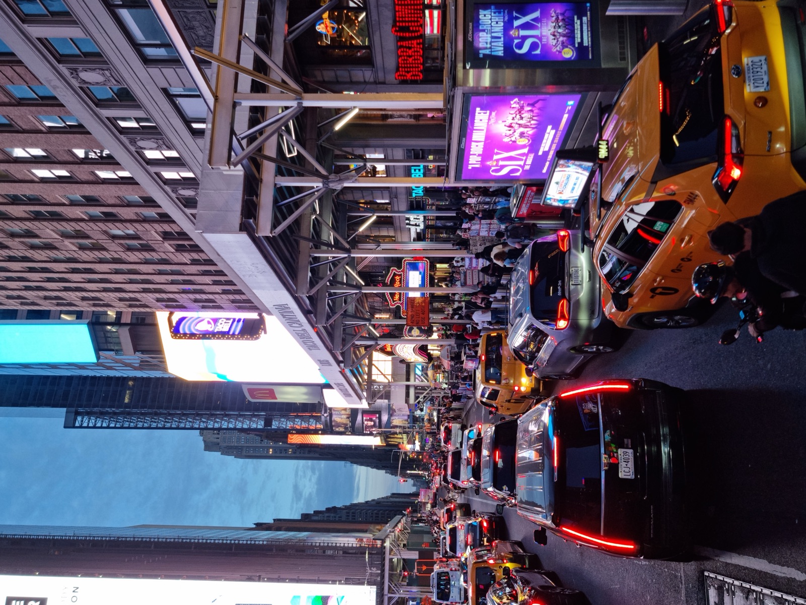 Yellow cabs and traffic stopped at the lights in Times Square at night with lit signs and a Broadway show billboard above