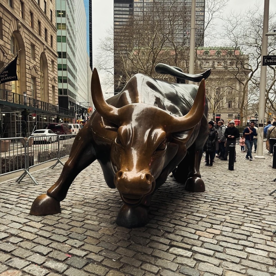 The bronze Charging Bull sculpture on the cobblestones near Wall Street, head lowered, surrounded by tourists