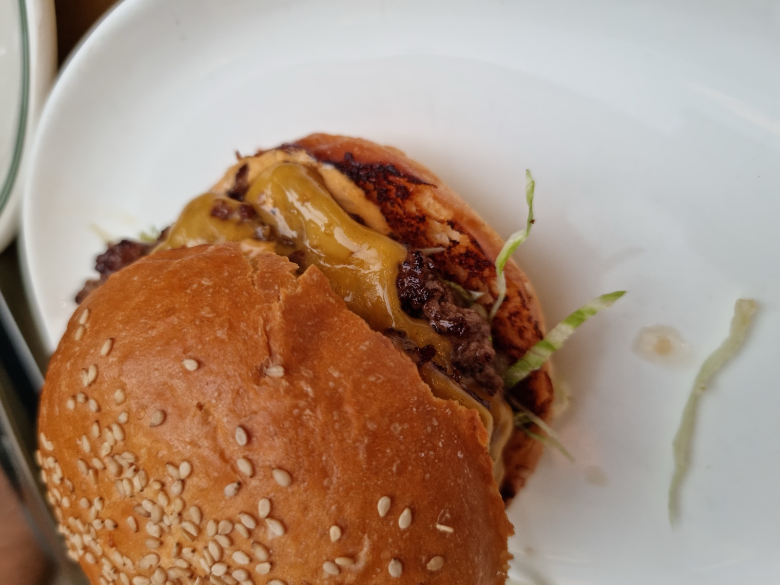 A cheeseburger on a sesame bun on a white plate, the melted cheese and patty visible under the bun