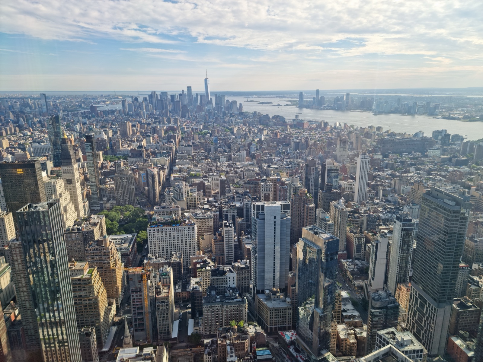 The view south from the Empire State Building over Midtown to the Lower Manhattan towers and the harbor beyond, under a hazy evening sky