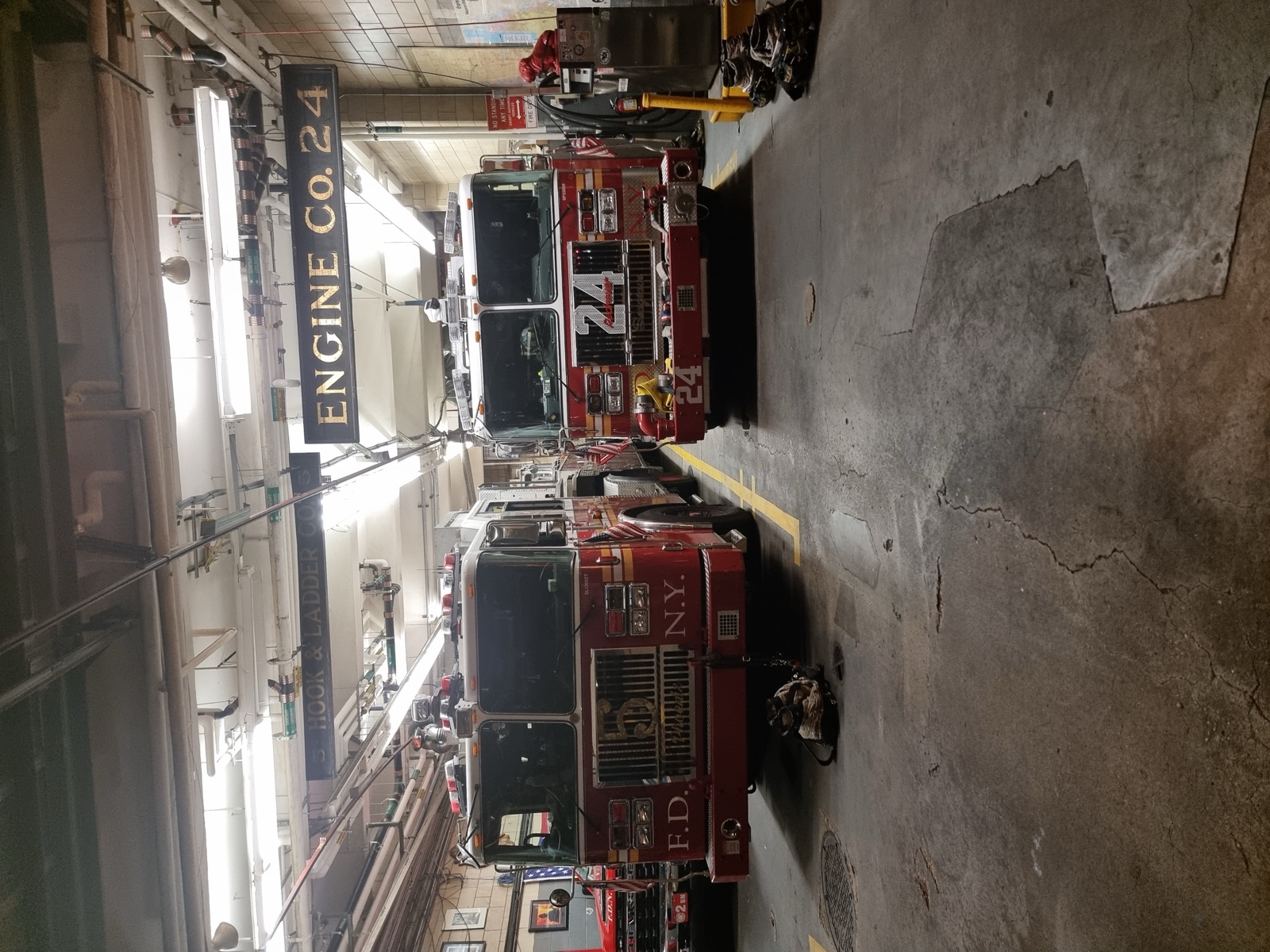 Two red fire engines parked nose out on the apparatus floor of a New York firehouse, with ENGINE CO. 24 lettered on the wall above them