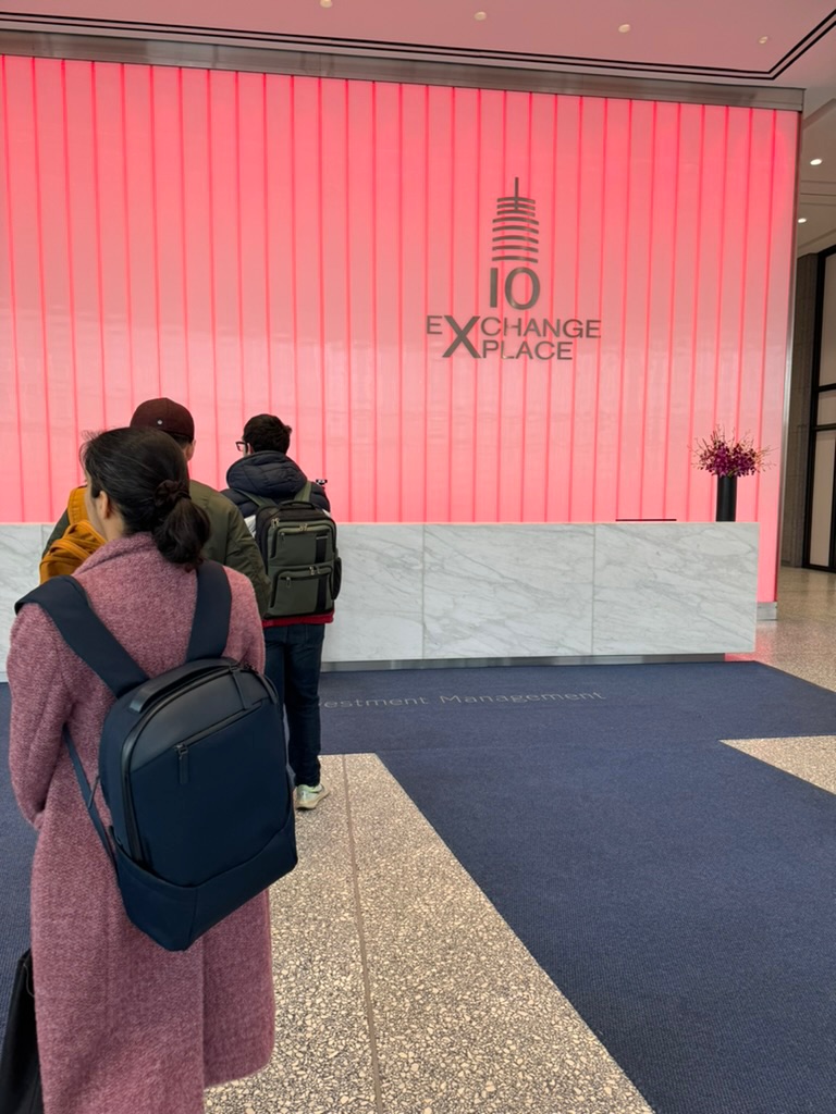 A marble reception desk lit deep pink in the lobby of 10 Exchange Place in Jersey City, people with backpacks walking toward it