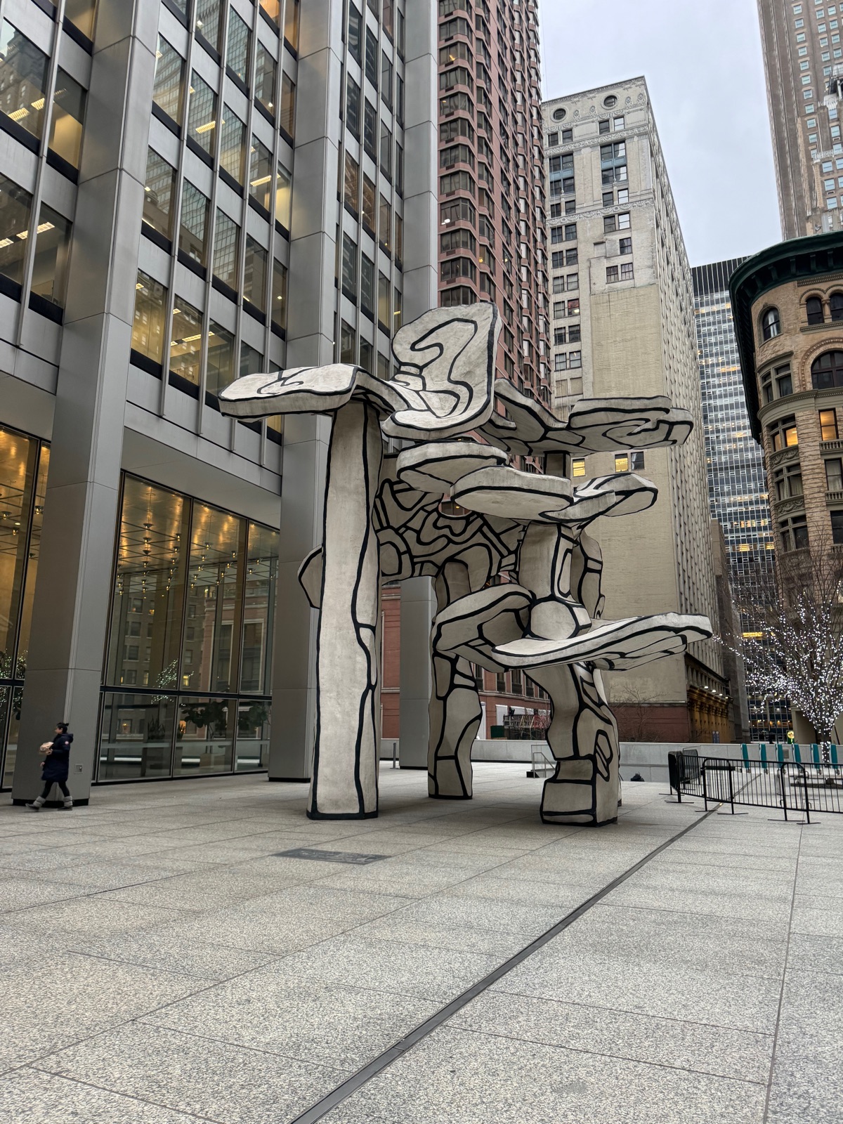 Jean Dubuffet's Group of Four Trees, a four-story white sculpture with heavy black outlines, standing on an empty paved plaza with towers behind
