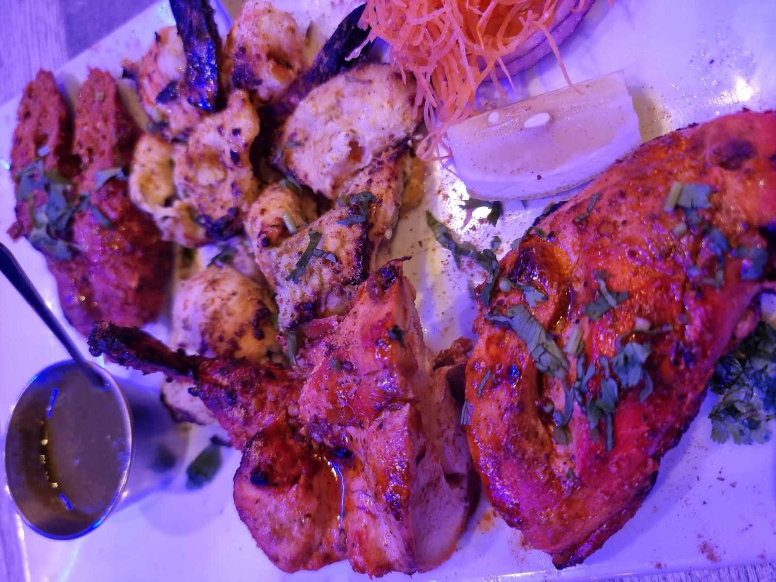 A platter of grilled seafood and skewers on a dark table under strong purple and pink restaurant lighting