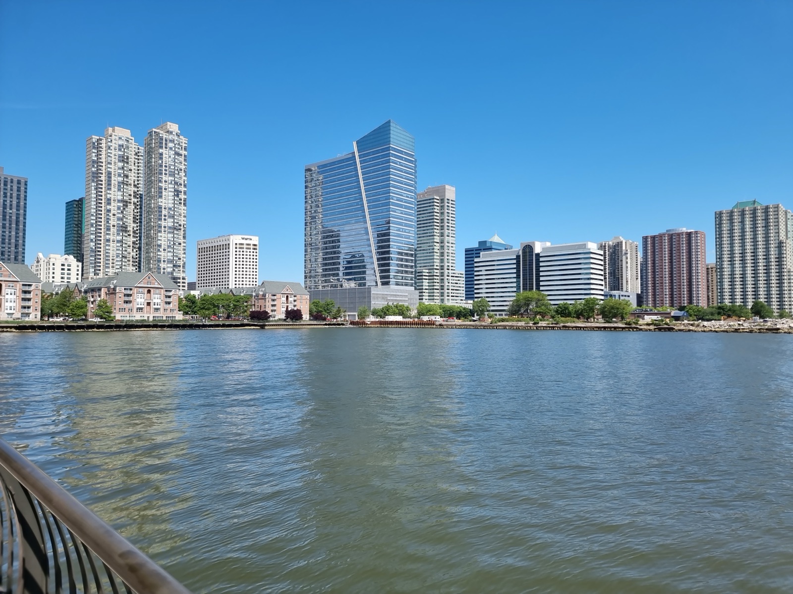 The glass and brick towers of the Jersey City waterfront seen low across the water from the end of a pier