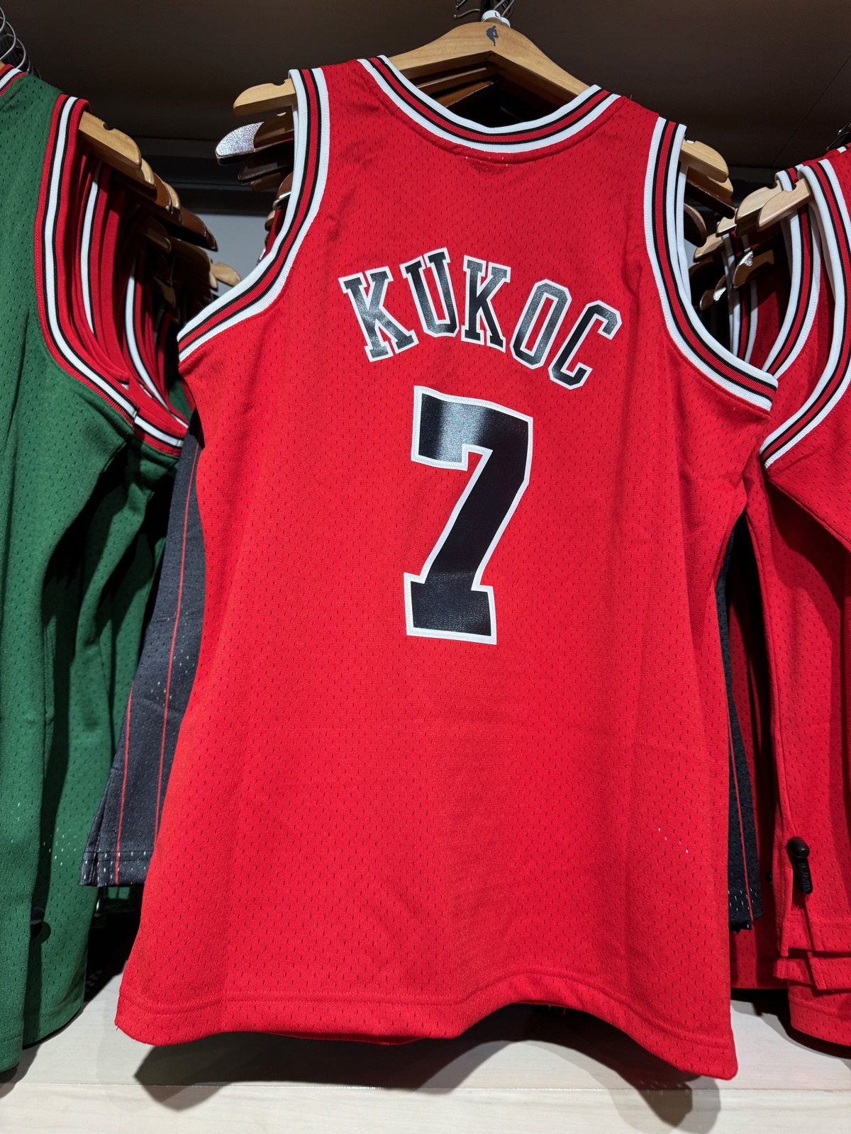 A red Chicago Bulls jersey printed KUKOC 7 hanging on a rail in a shop among other jerseys