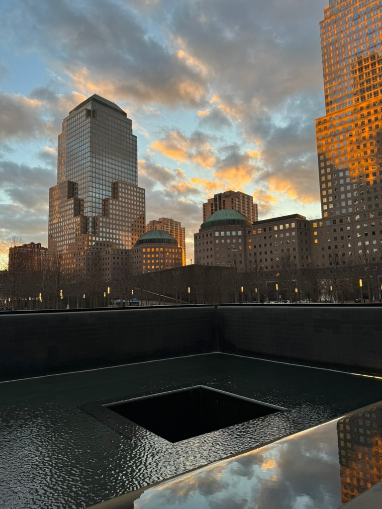 The September 11 Memorial pool at golden hour, the surrounding towers catching an orange sunset