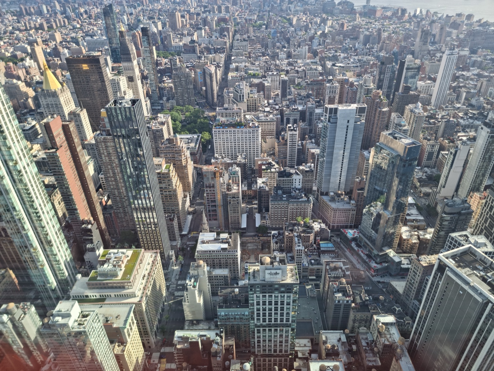 A steep view straight down from the Empire State Building onto the roofs and streets of Midtown, the avenues running away as narrow canyons