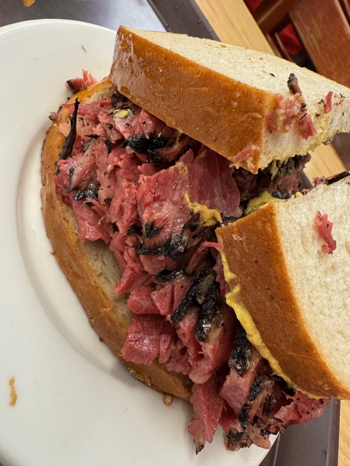 A hand-cut pastrami sandwich on rye bread on a white plate, the meat piled thickly between two slices