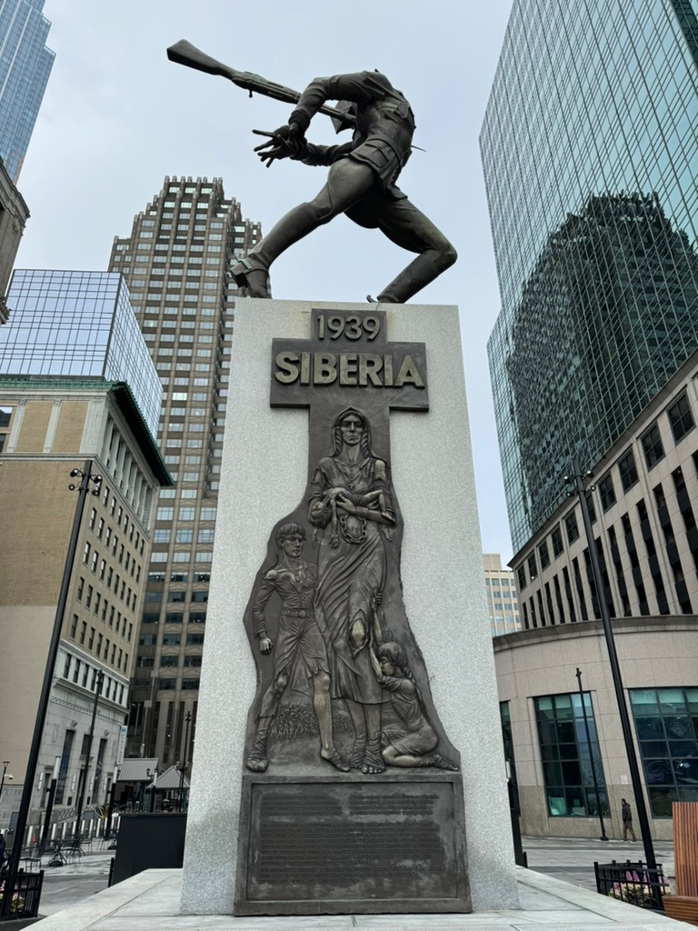 A dramatic bronze memorial in Exchange Place, Jersey City: a leaping figure holding a rifle overhead atop a granite plinth carved with the words 1939 Siberia and a relief of a mother and children
