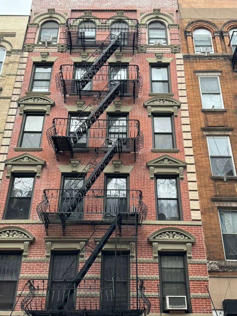 A red-brick Lower East Side tenement facade covered in ornate black iron fire escapes