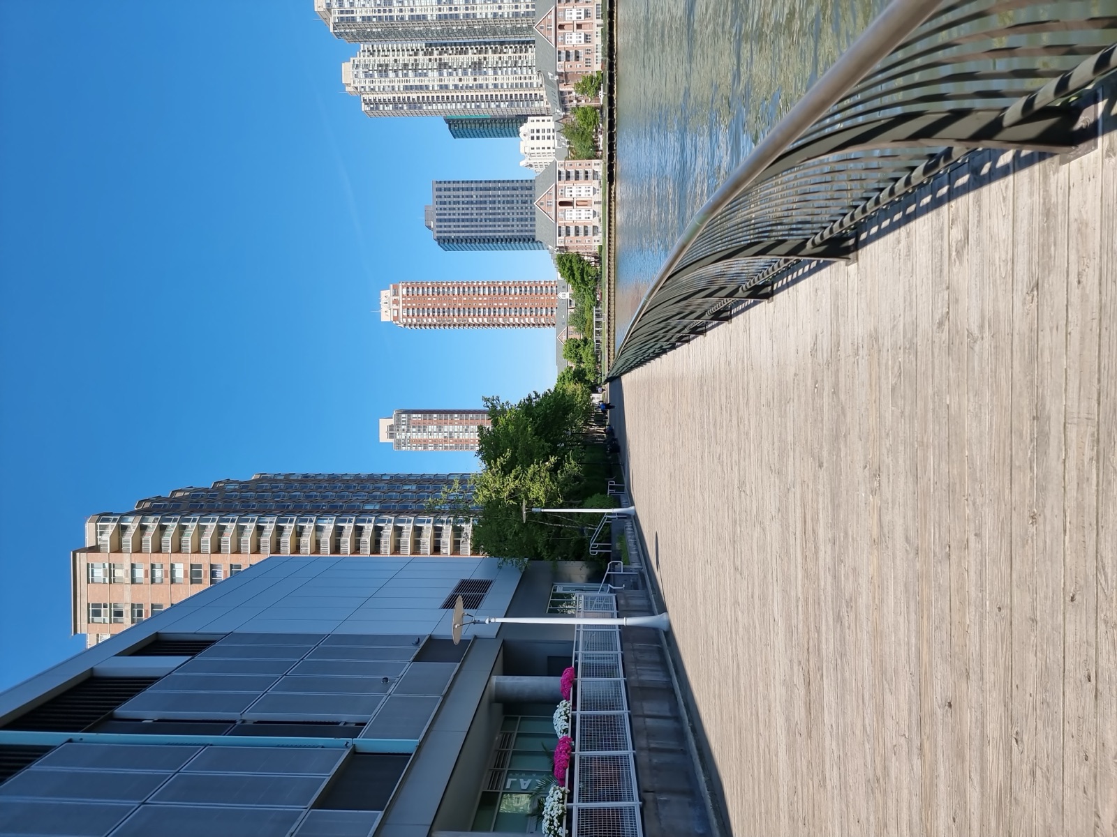 A timber boardwalk running along the Jersey City waterfront with residential towers on the left and the Hudson on the right