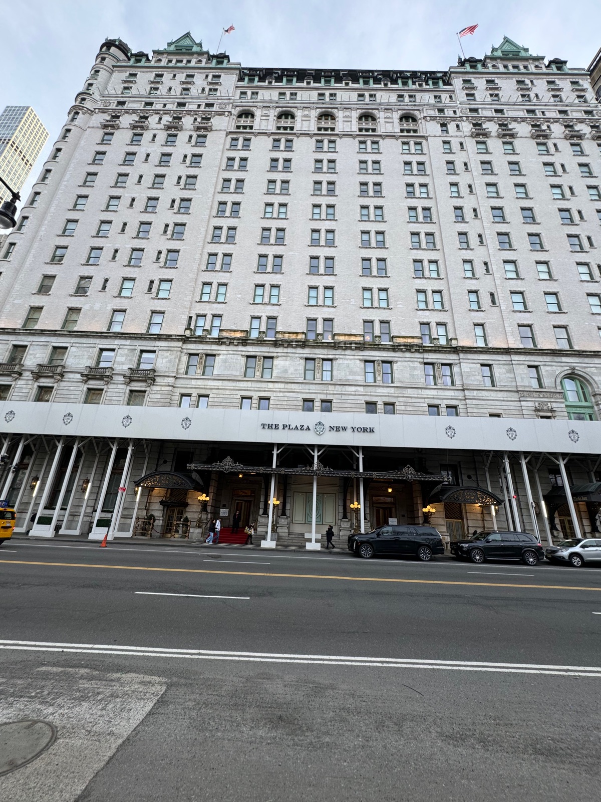 The pale stone facade of The Plaza hotel with its name in capitals along the front and awnings over the entrance, seen from across the street