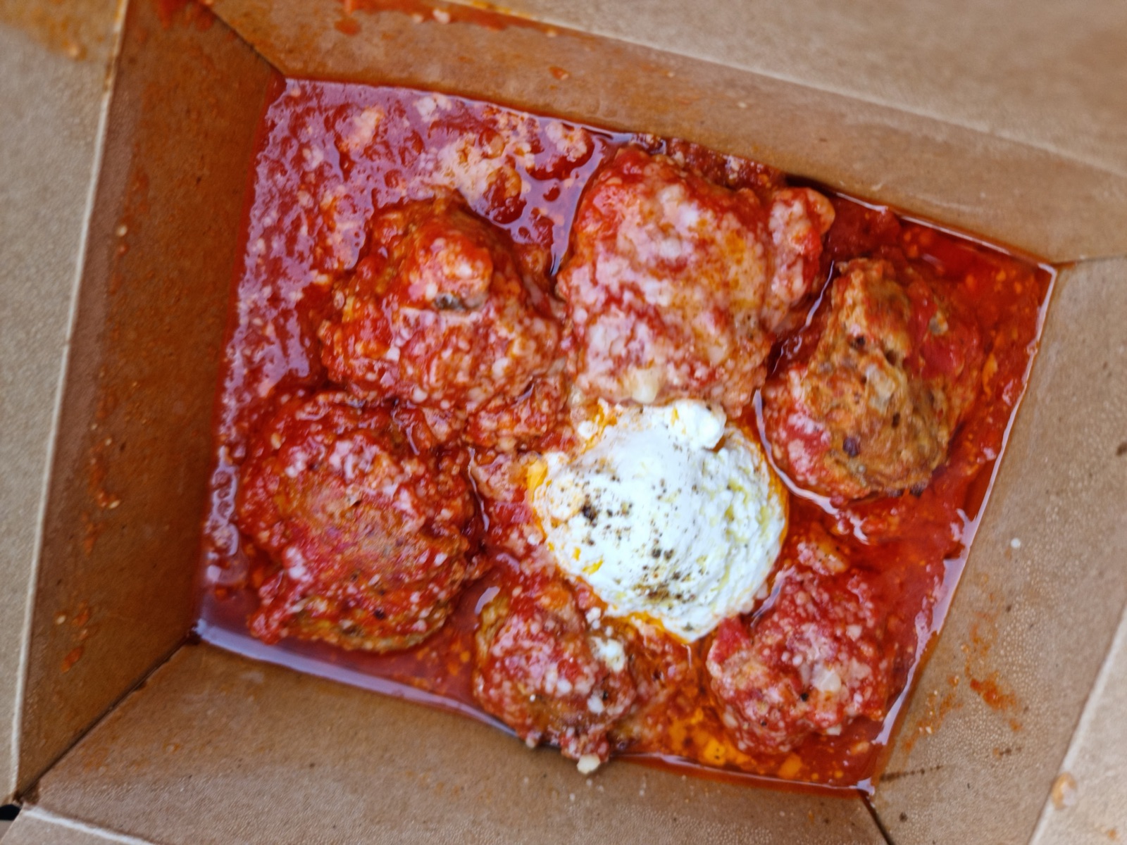 A thick square Sicilian-style pizza slice in a cardboard box, heavy with tomato sauce and a spoonful of ricotta on top