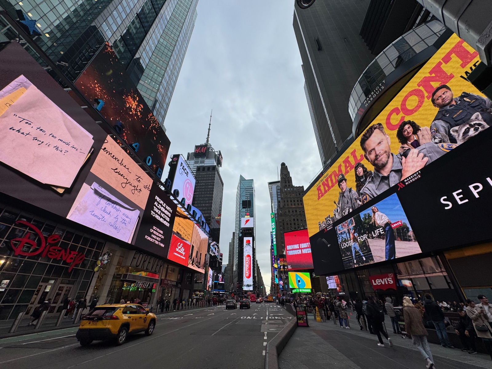A wide view down Seventh Avenue through Times Square with a yellow cab in the foreground and lit billboards on every building