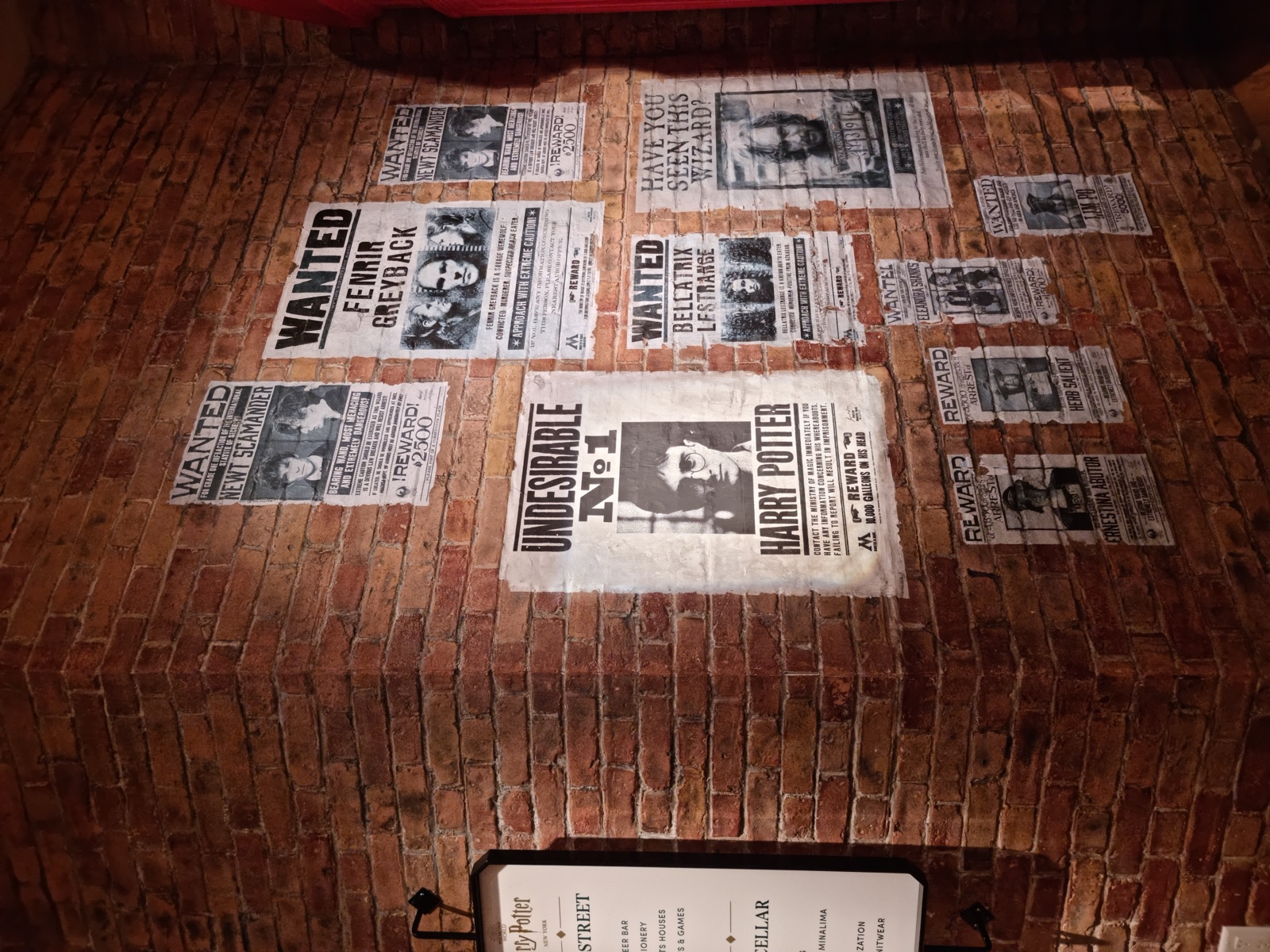 A brick wall covered with WANTED posters in the style of the Harry Potter films, including one reading UNDESIRABLE No 1 with Harry Potter's face, beside a directory board for Harry Potter New York